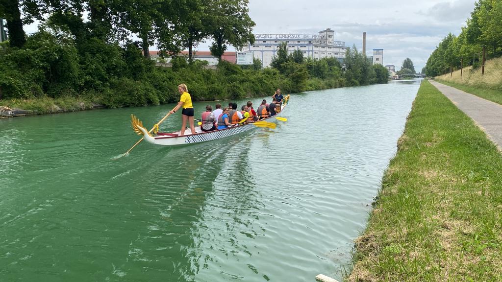le dragon boat navigue sur la coulée verte avec ses matelots à bord. Une personne se tient debout et mène le dragon boat avec une rame
