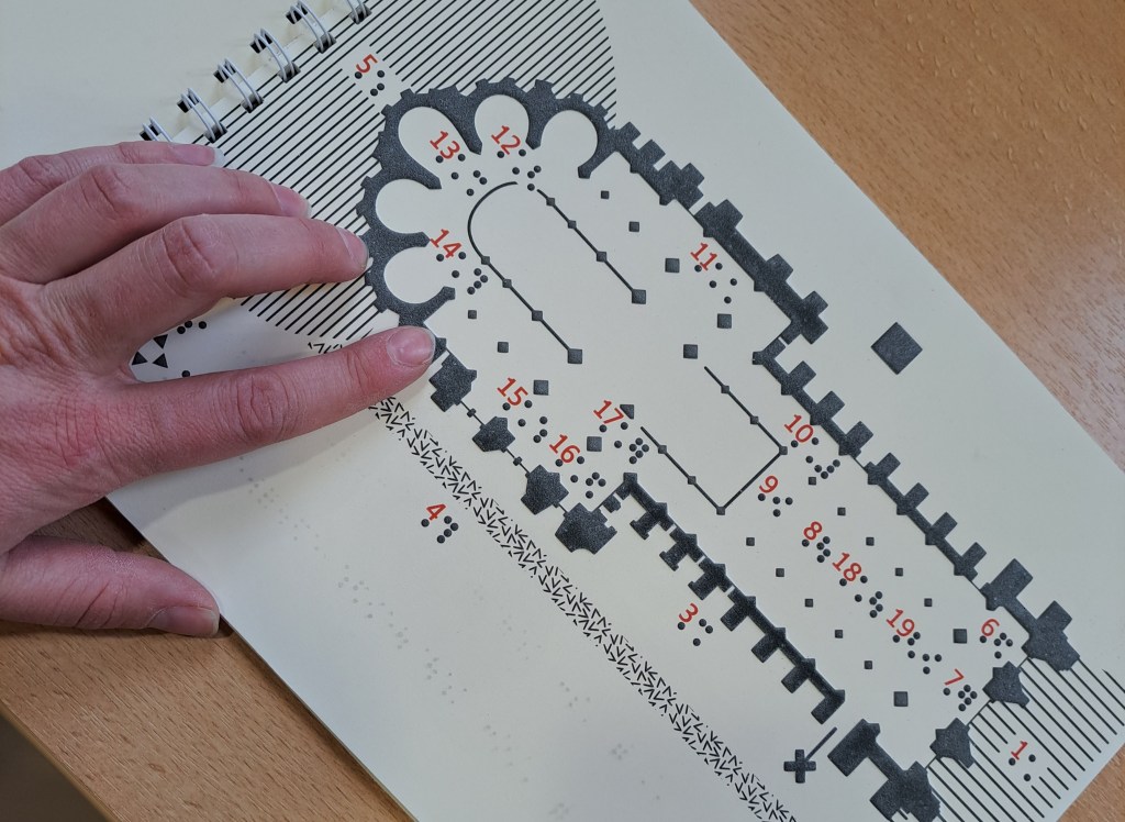 Une main et posée sur un plan tactile en thermogonflé. il s'agit de la cathédrale notre-dame de reims