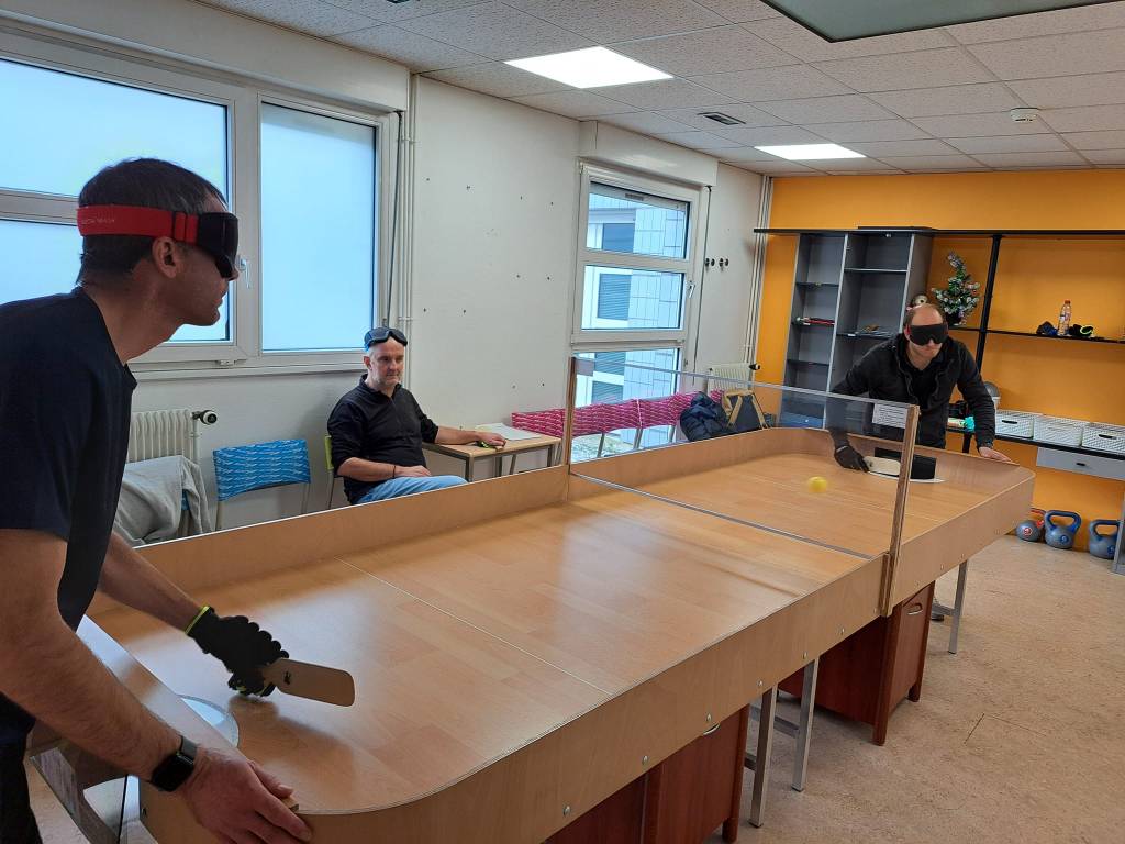 deux personnes portent un gant et un bandeau. elles tiennent une raquette dans leur main gantée
elles jouent sur une grande table en bois
